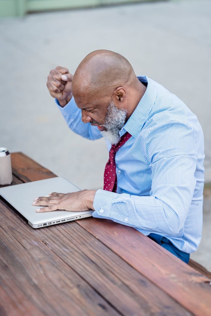 Concentrated bald senior bearded male entrepreneur sitting at table with closed laptop and thinking over project